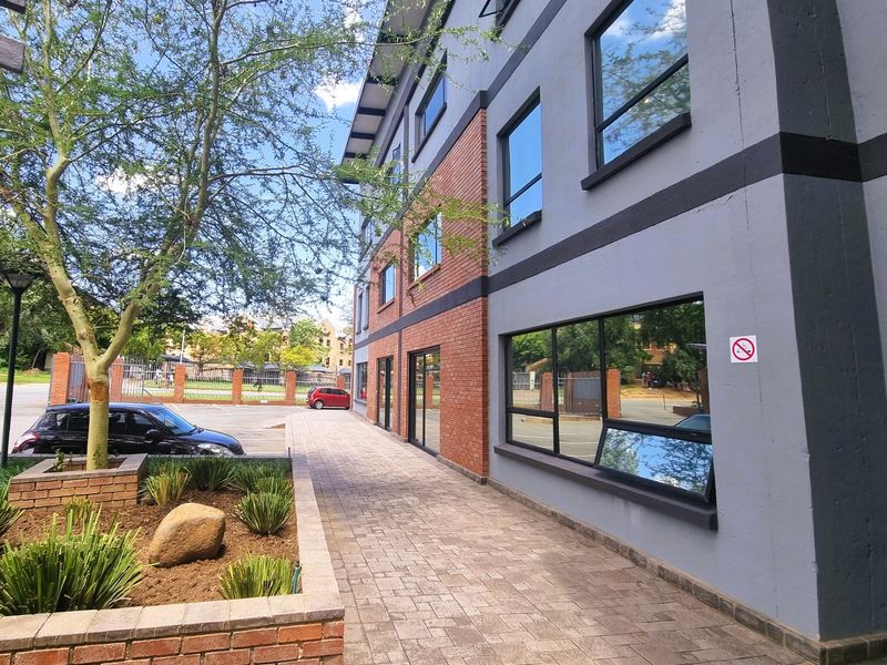Exterior view of a modern office building featuring a brick and painted facade, paved walkway, and landscaped planter area.
