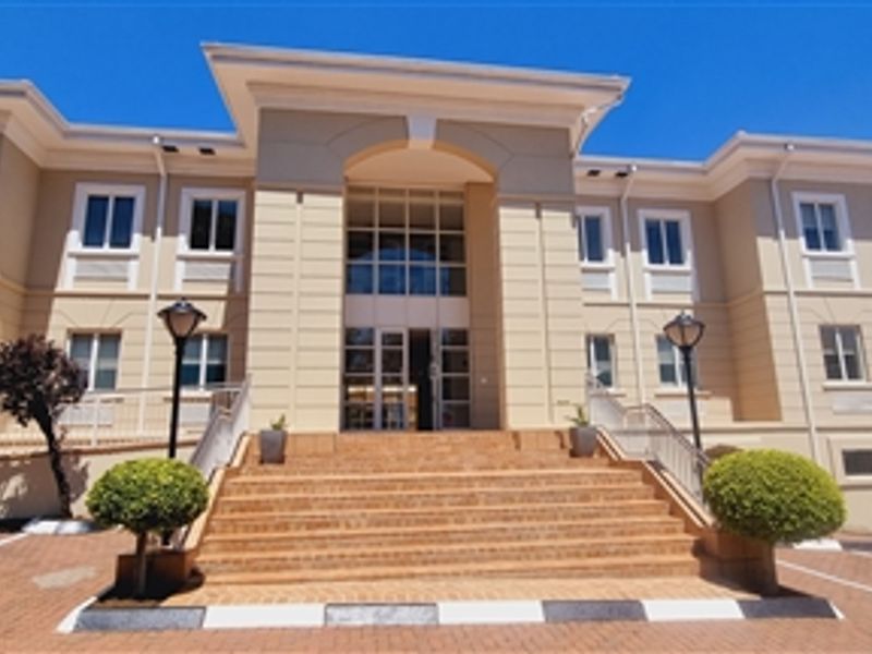 A professional front elevation of a multi-story office building featuring a grand brick staircase entrance, paved parking area, and well-maintained exterior facade.