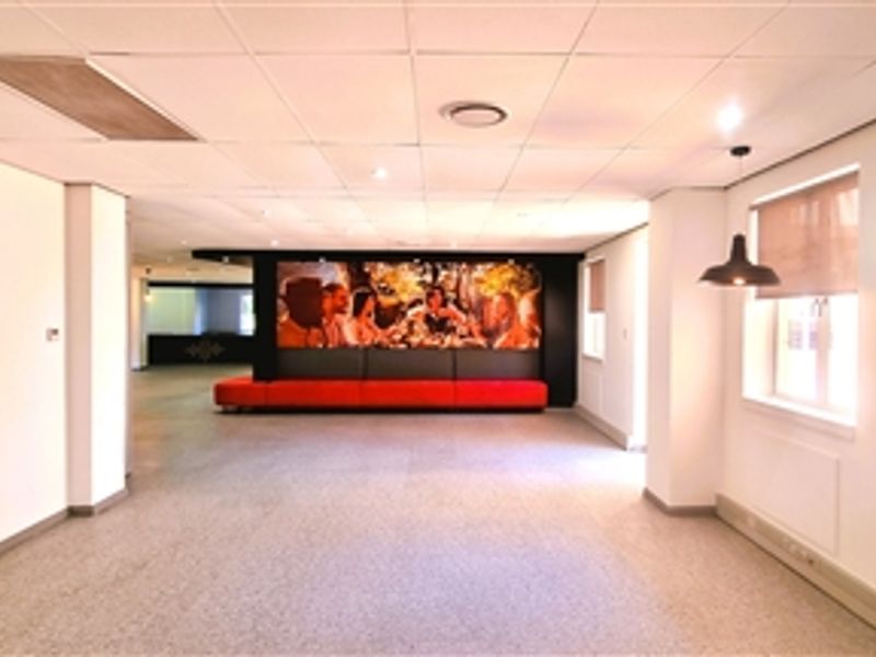 Spacious open-plan office area featuring a suspended ceiling, recessed lighting, and integrated bench seating against a feature wall.