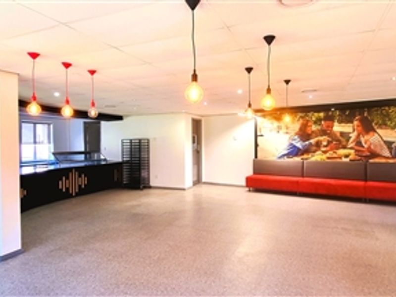 Spacious open-plan office breakout area featuring a built-in service counter, integrated bench seating, modern pendant lighting, and durable terrazzo flooring.