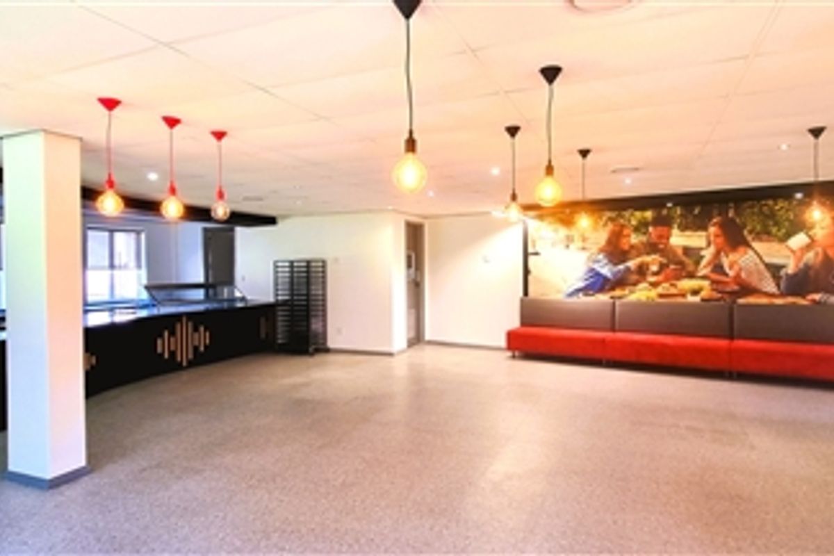 Spacious open-plan office breakout area featuring a built-in service counter, integrated bench seating, modern pendant lighting, and durable terrazzo flooring.