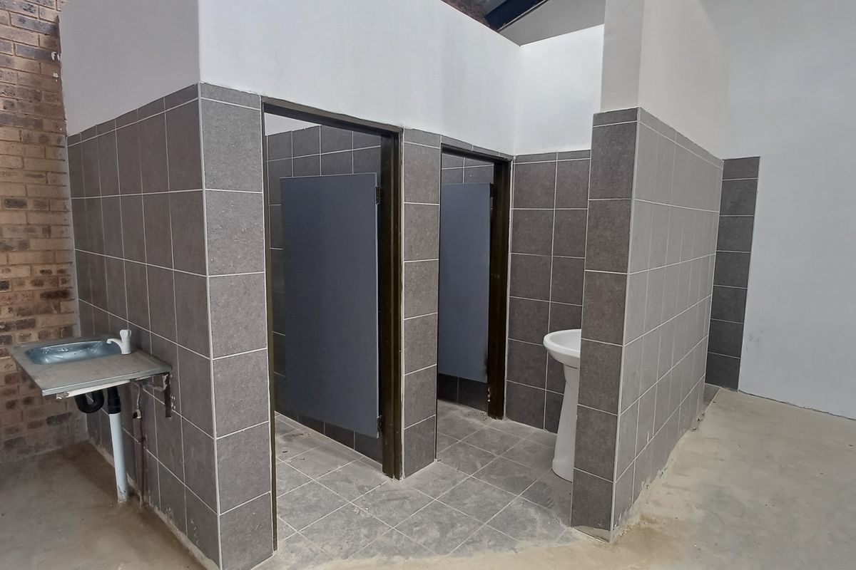 Industrial-style restroom facility featuring tiled partitions, two private cubicles, a pedestal basin, and a stainless steel utility sink.