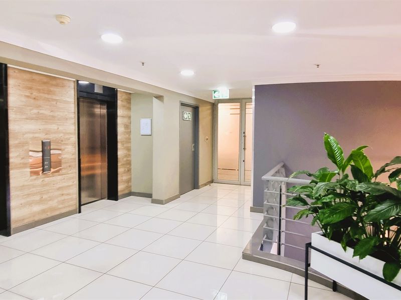 A modern, well-maintained office building lobby featuring dual elevators, polished tile flooring, and access to a staircase.