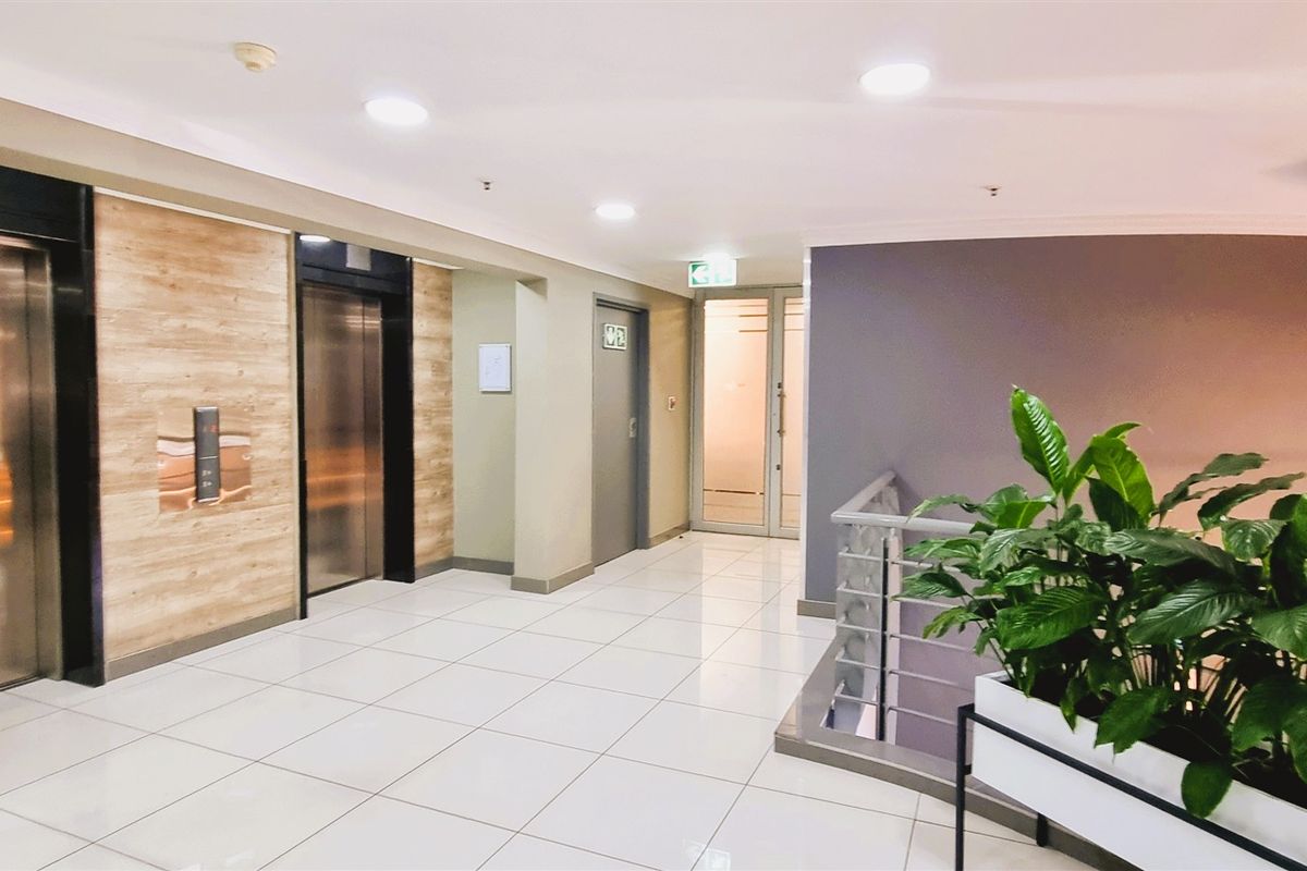 A modern, well-maintained office building lobby featuring dual elevators, polished tile flooring, and access to a staircase.
