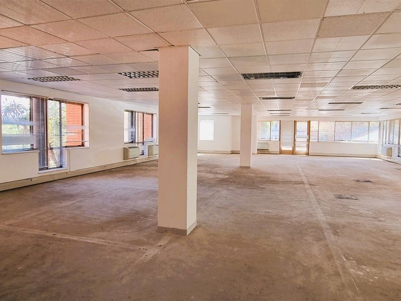 A large, open-plan office space featuring suspended ceilings, structural columns, and extensive natural light through multiple windows, currently in need of refurbishment.