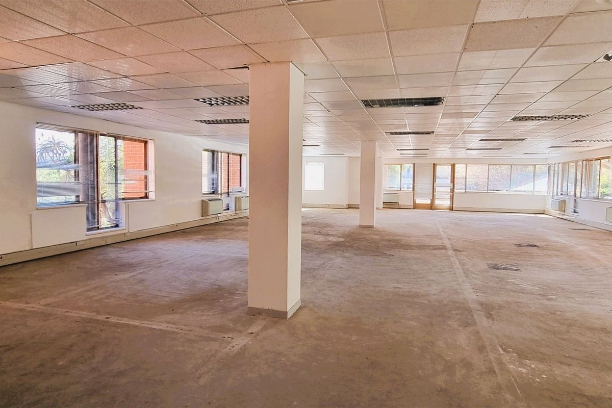 A large, open-plan office space featuring suspended ceilings, structural columns, and extensive natural light through multiple windows, currently in need of refurbishment.