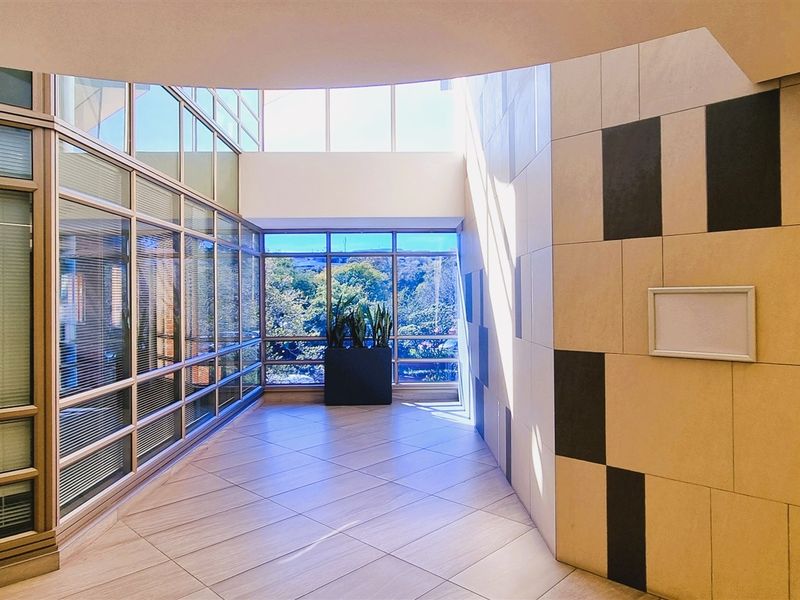 Modern office lobby or circulation area featuring extensive glass curtain walls, natural light from a skylight, and contemporary tiled wall finishes.