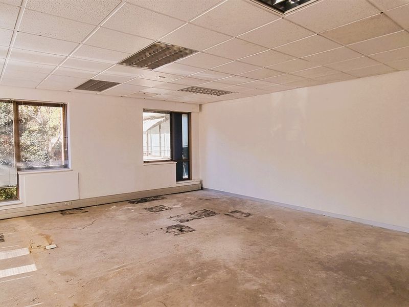 An empty office space featuring a suspended ceiling with recessed lighting and large windows, currently requiring flooring repairs.