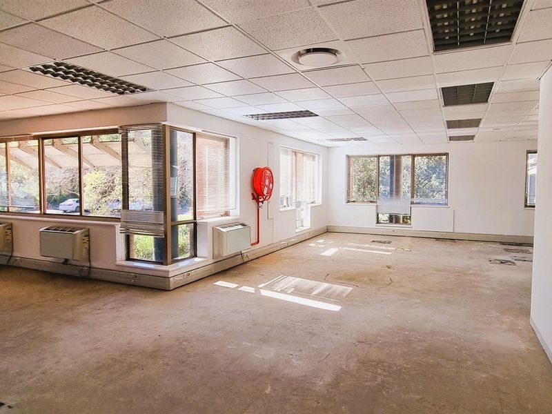 A spacious, vacant open-plan office area featuring a suspended ceiling, large windows for natural light, and integrated air conditioning units.