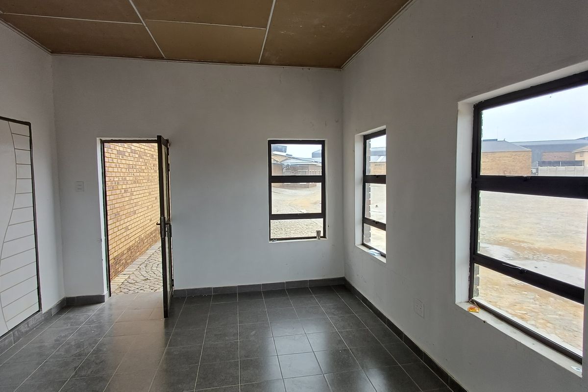 An empty interior room featuring tiled flooring, multiple windows providing natural light, and a door leading to an exterior paved area.