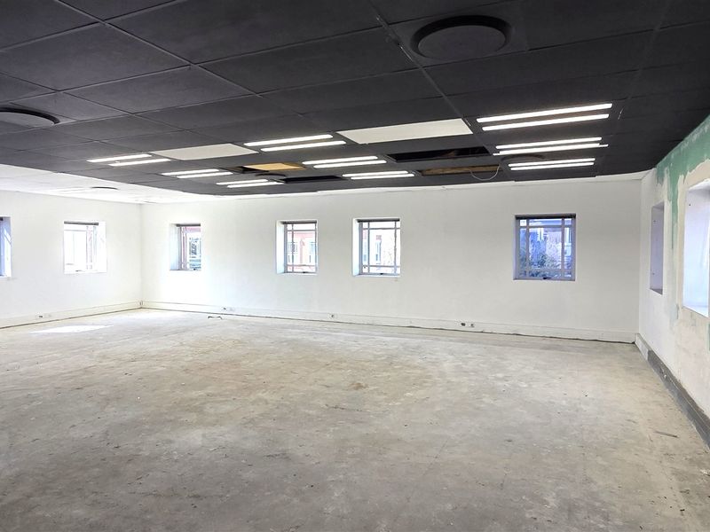 Spacious open-plan office area featuring a suspended ceiling, recessed lighting, and security bars on windows, currently in a shell condition requiring finishing.