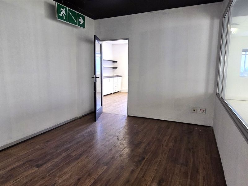 Empty office space featuring laminate flooring, a glass partition wall, and an emergency exit sign, providing a clean and functional workspace.