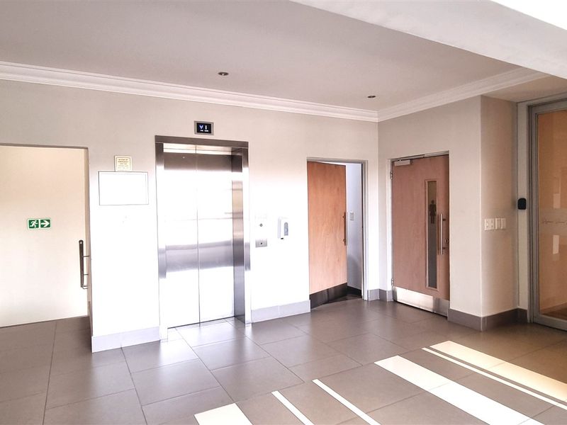 A clean and professional office building lobby featuring tiled flooring, a modern elevator, and glass-paneled entry doors with recessed lighting.