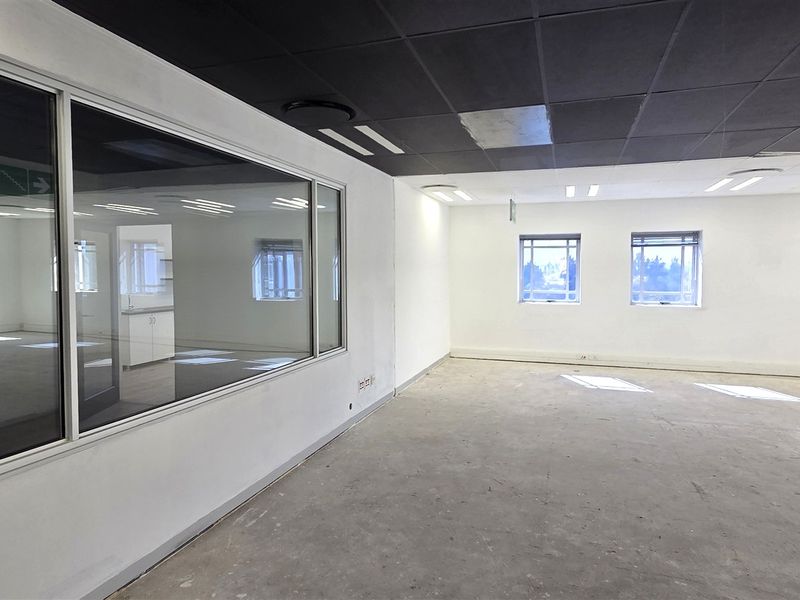 An empty, open-plan office space featuring a suspended ceiling, recessed lighting, and an internal glass partition wall with large windows.
