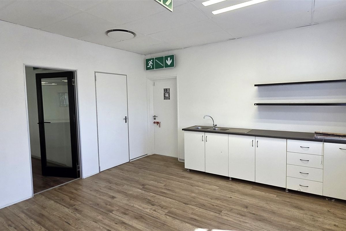 A clean, functional office kitchenette featuring white cabinetry, a stainless steel sink, laminate countertops, and floating shelves, set against a neutral interior.