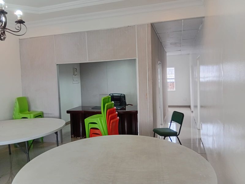 An office interior featuring a partitioned workspace, tiled flooring, and a connecting hallway with neutral wall finishes.