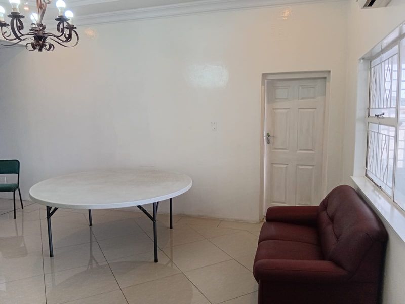 A bright office space featuring tiled flooring, a decorative chandelier, and a secure window with burglar bars.