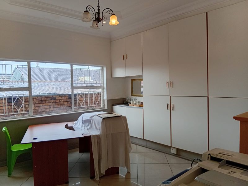 Office space featuring extensive built-in white cabinetry, tiled flooring, and large windows with security bars, providing a functional workspace environment.