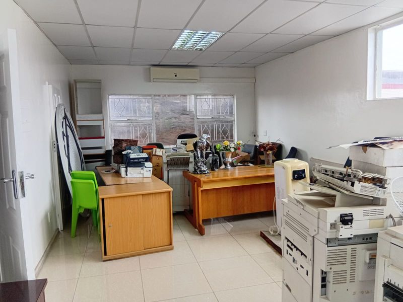 A functional office space featuring tiled flooring, a drop ceiling with integrated lighting, and a wall-mounted air conditioning unit.