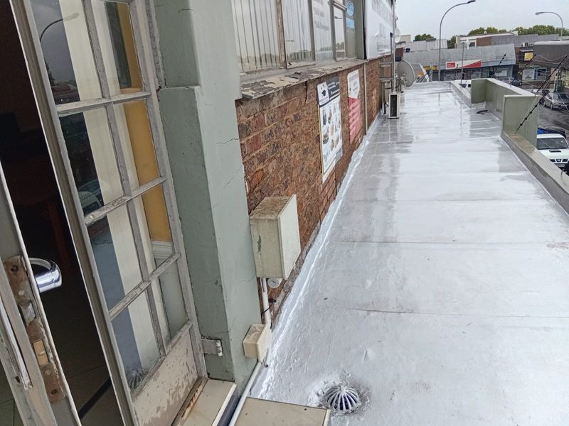 An exterior balcony area featuring a waterproofed surface, brick facade, and access via a glass-paned door.