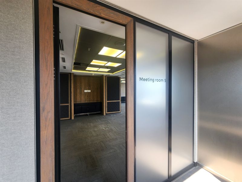 A modern, professional meeting room featuring frosted glass partitioning, wood veneer accents, recessed ceiling lighting, and integrated floor power outlets.