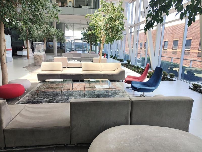 Spacious modern office lobby or breakout area featuring floor-to-ceiling windows, tiled flooring, and integrated indoor greenery.