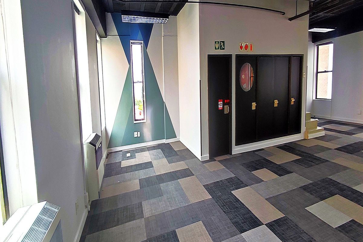 A bright, open-plan office space featuring modern carpet tiles, exposed industrial-style ceilings, and built-in storage cabinets.