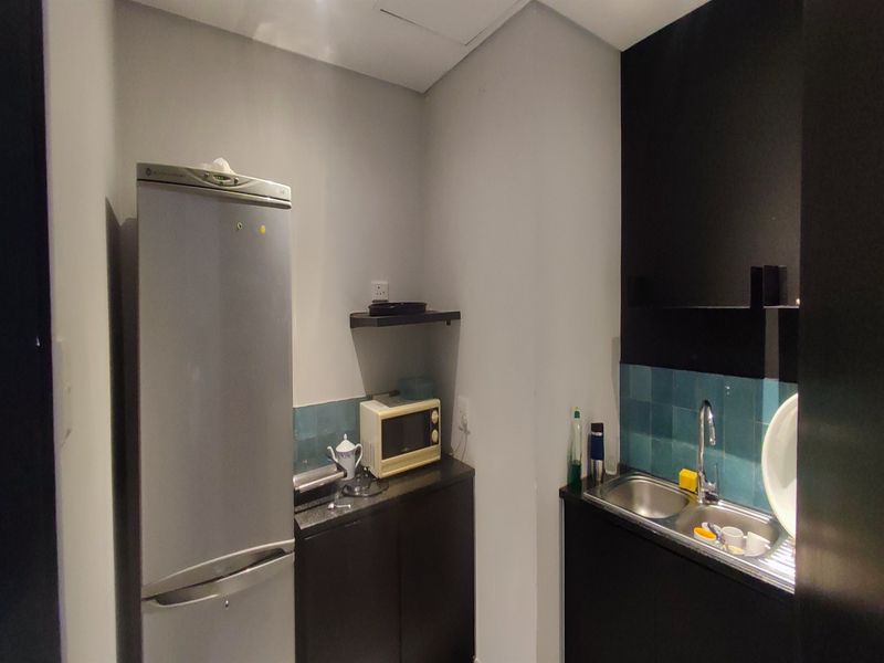 A compact office kitchenette featuring dark cabinetry, a stainless steel sink, tiled backsplash, and functional counter space for basic food preparation.