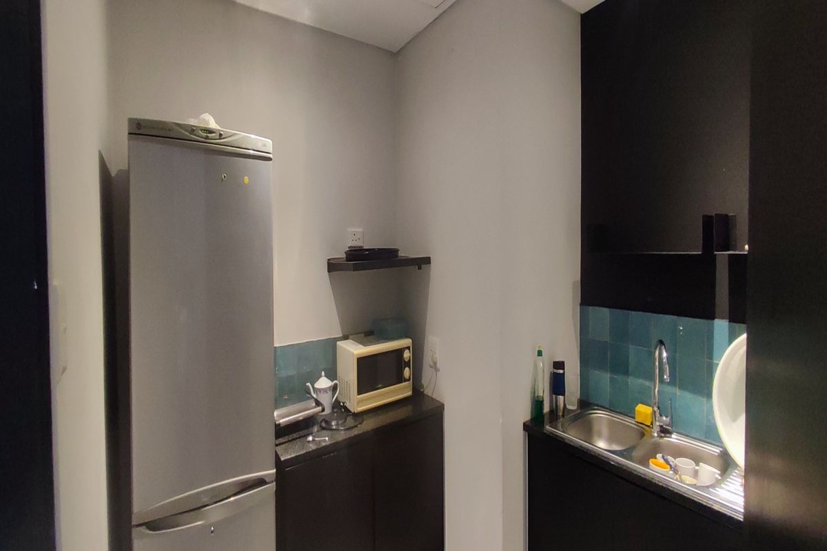 A compact office kitchenette featuring dark cabinetry, a stainless steel sink, tiled backsplash, and functional counter space for basic food preparation.