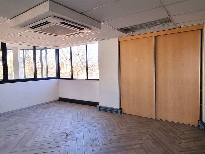 Empty office space featuring herringbone flooring, large windows for natural light, built-in storage cupboards, and a recessed ceiling air conditioning unit.