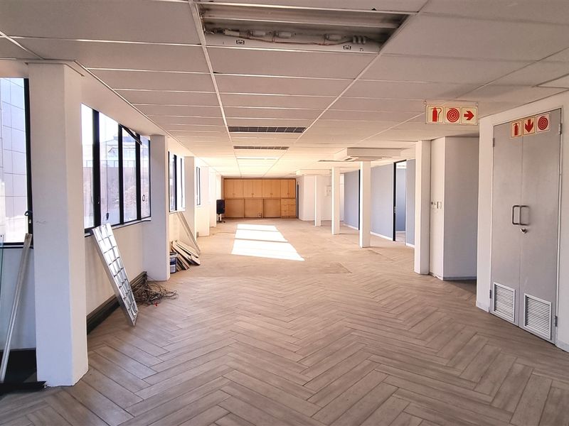 Spacious open-plan office area featuring herringbone tile flooring, large windows for natural light, built-in storage cabinetry, and a functional fire exit.