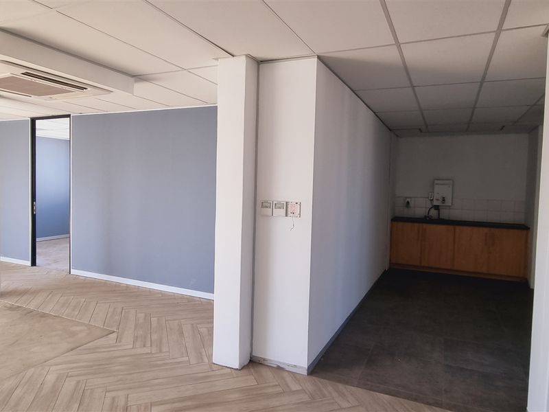 Open plan office space featuring herringbone flooring, a suspended ceiling with integrated air conditioning, and a small kitchenette area.