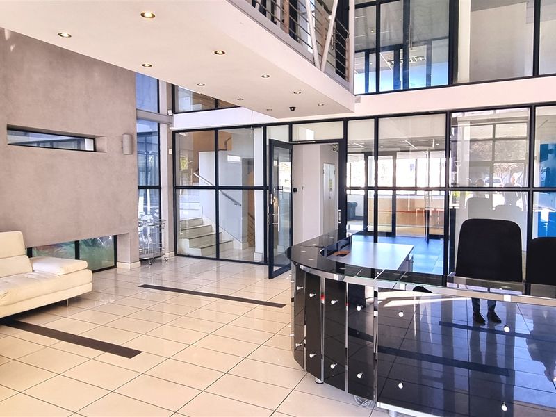 Modern office reception area featuring a sleek reception desk, glass partitioning, high ceilings with a mezzanine level, and polished tiled flooring.