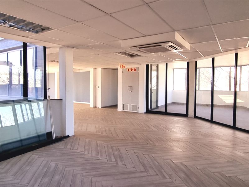 Spacious, modern open-plan office area featuring herringbone tile flooring, suspended ceilings, integrated air conditioning, and extensive floor-to-ceiling glass partitioning for natural light.