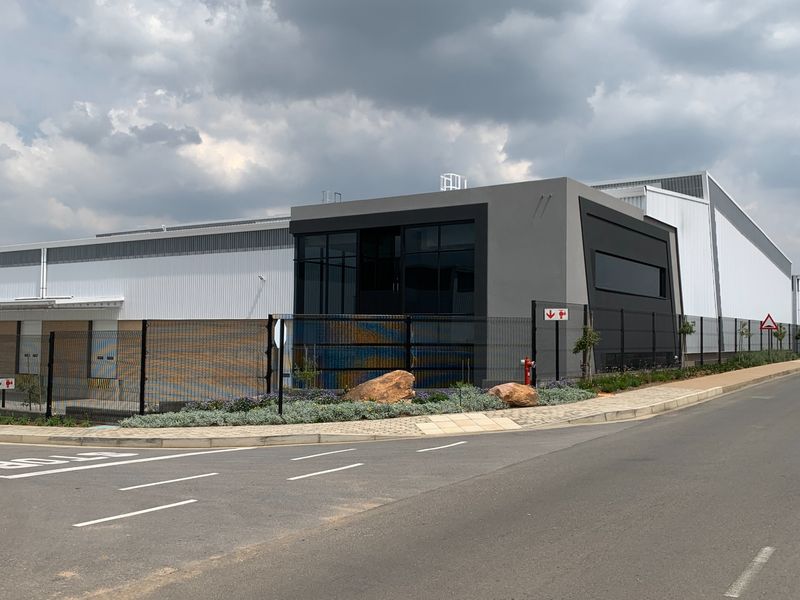 Modern industrial facility featuring contemporary metal cladding, large glass facade, secure perimeter fencing, and convenient roller shutter access points.