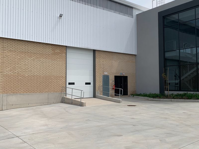 Industrial exterior view featuring a concrete loading ramp, roller shutter door, and modern glass facade with metal and brick cladding.