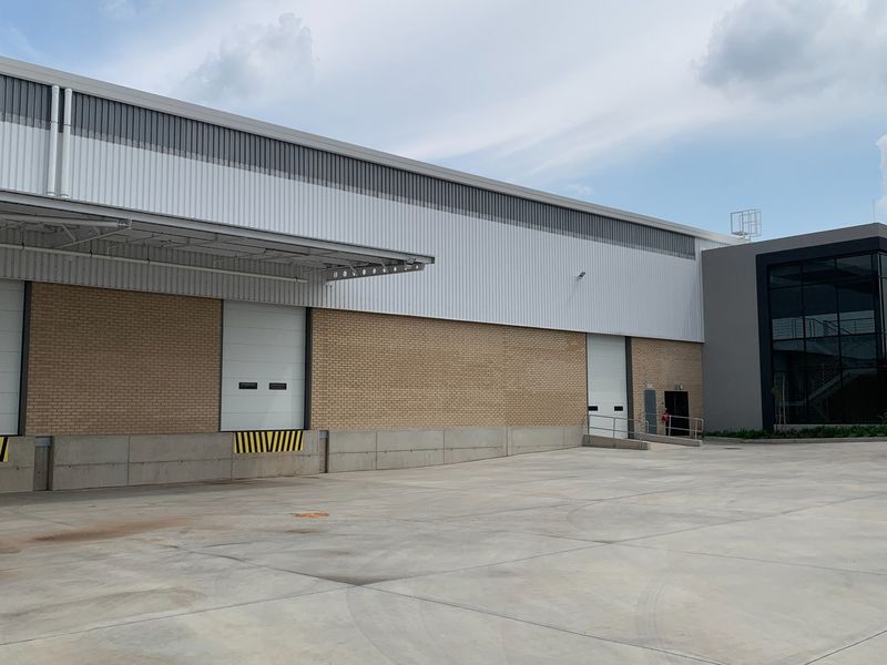 Industrial warehouse exterior featuring a concrete loading yard, multiple roller shutter doors, and modern metal and brick facade construction.