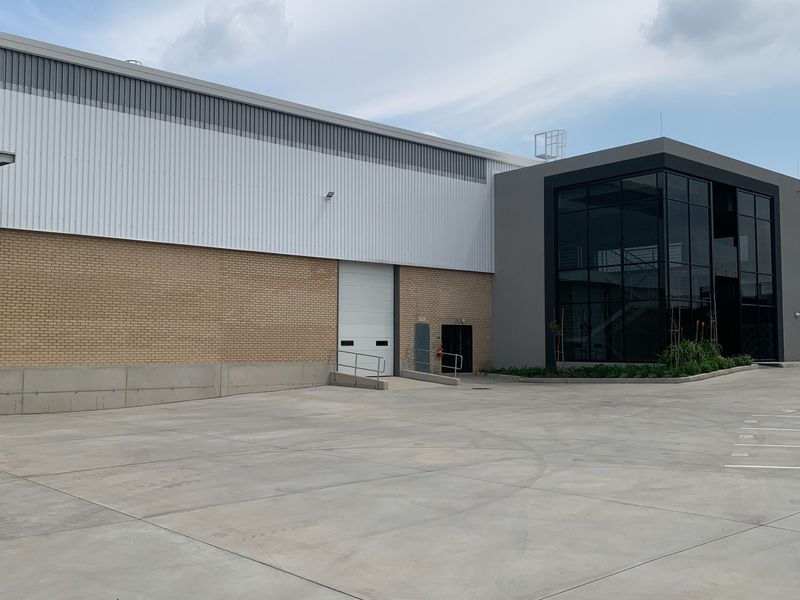 Modern industrial facility featuring a large roller shutter door, concrete loading area, and a contemporary glass-fronted office or entrance section.