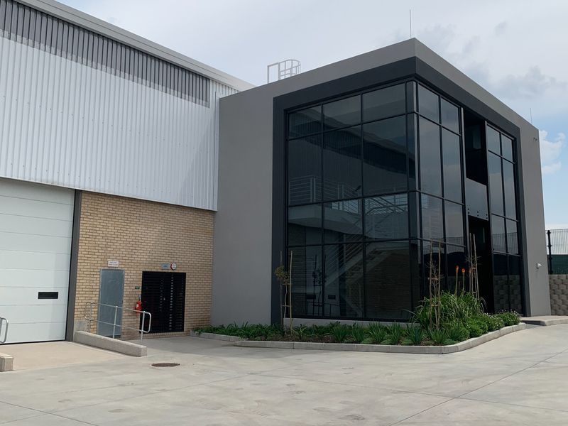 Modern industrial facility featuring a combination of brick and metal cladding, large glass curtain wall facade, and a functional roller door entrance.