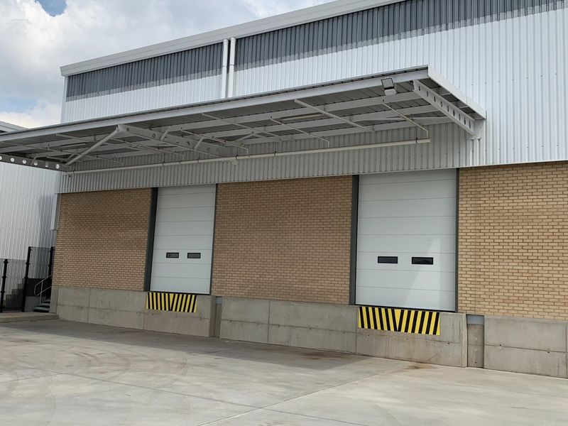 Industrial warehouse exterior featuring two loading bays with roller shutter doors, a protective canopy, and a durable concrete loading apron.