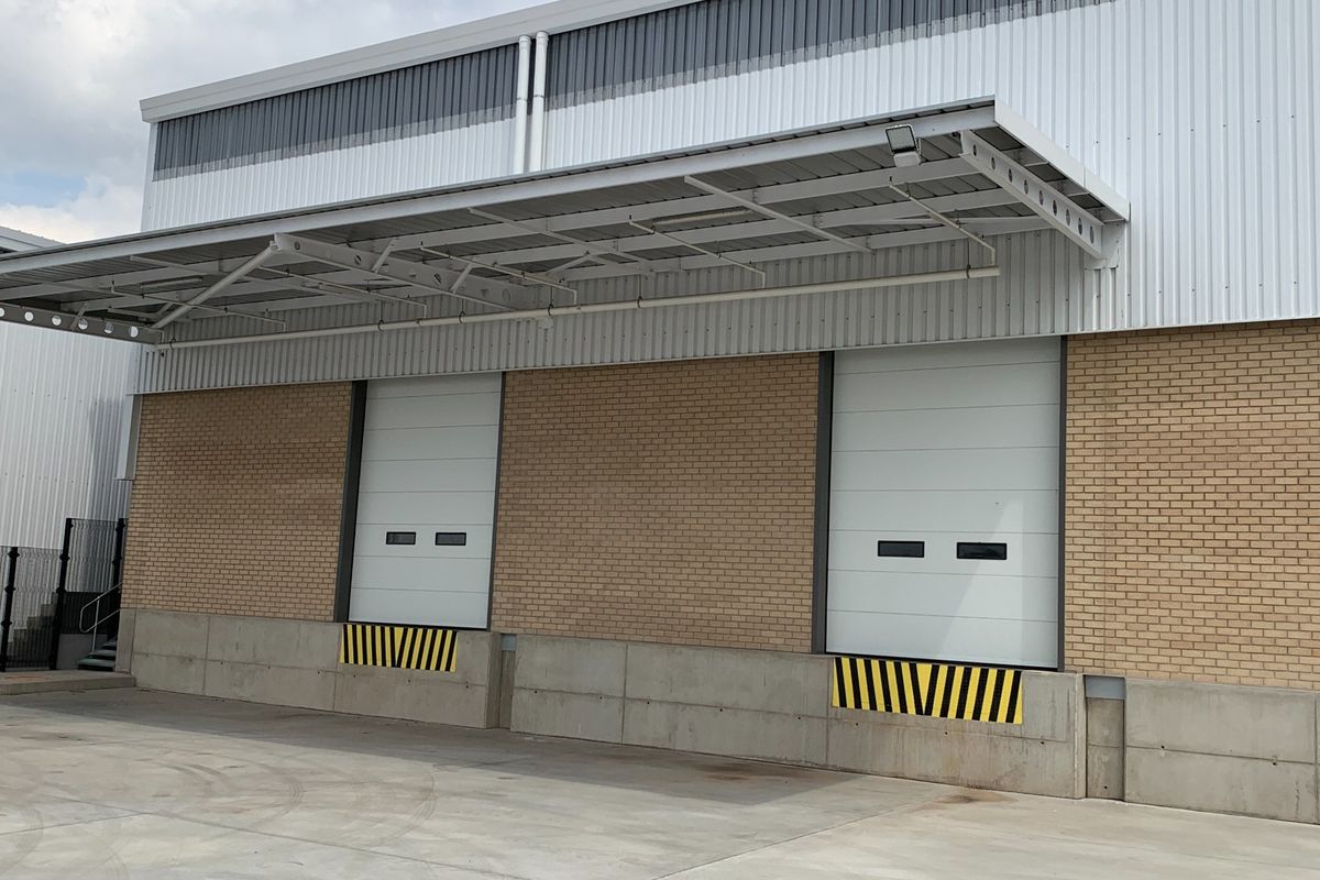 Industrial warehouse exterior featuring two loading bays with roller shutter doors, a protective canopy, and a durable concrete loading apron.