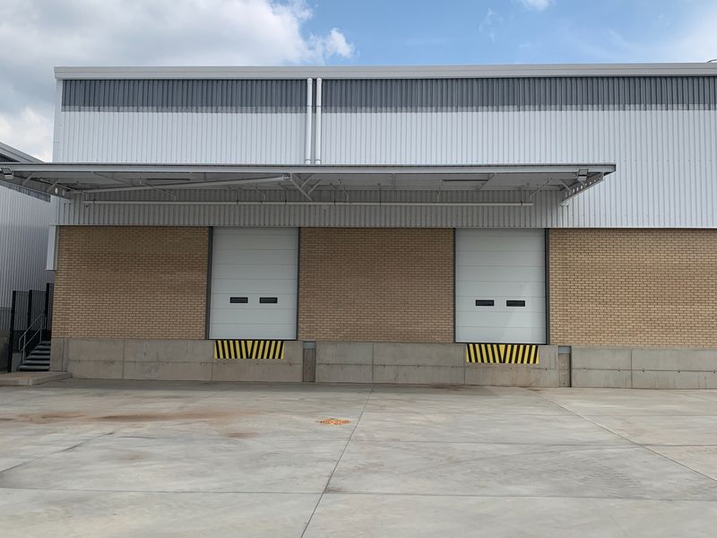 Industrial warehouse exterior featuring two loading bays with roller shutter doors, a protective canopy, and a spacious concrete loading apron.