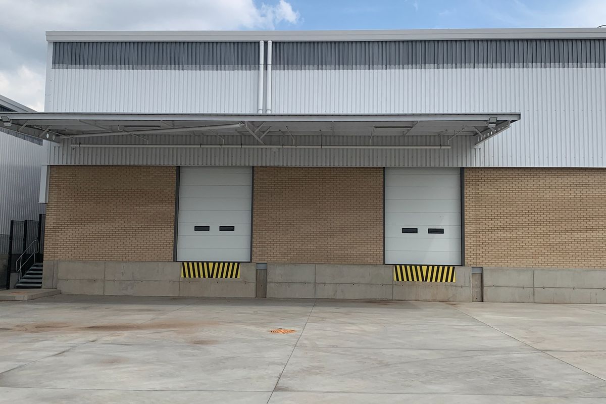 Industrial warehouse exterior featuring two loading bays with roller shutter doors, a protective canopy, and a spacious concrete loading apron.