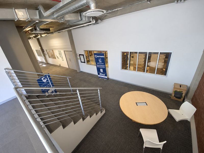 Modern industrial-style office space featuring an open-plan layout, exposed ceiling ductwork, a central staircase, and internal glass partitions overlooking adjacent work areas.
