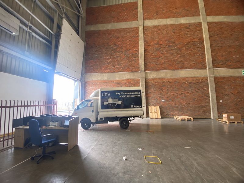 Spacious industrial warehouse unit featuring high ceilings, exposed brick walls, polished concrete flooring, and a large roller shutter door for vehicle access.