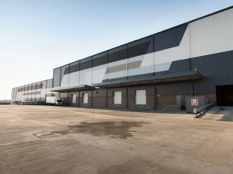 Large industrial warehouse facility featuring multiple loading docks, expansive concrete yard space, and modern metal cladding exterior.