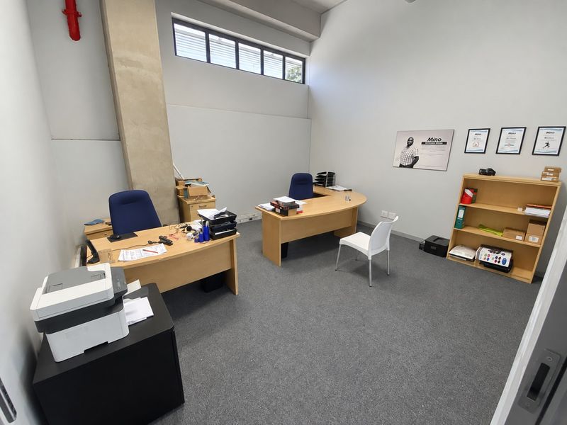 A functional industrial-style office space featuring high ceilings, exposed concrete structural elements, clerestory windows for natural light, and durable carpet flooring.