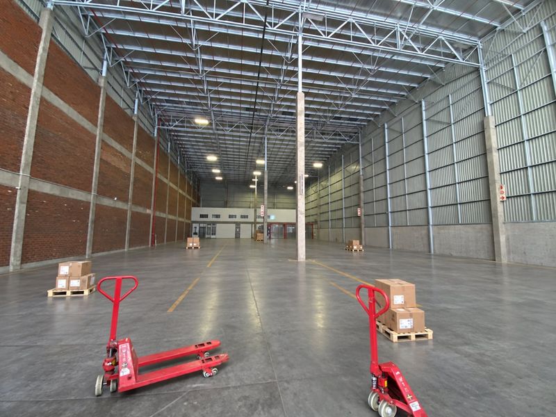 Spacious industrial warehouse unit featuring high ceilings with exposed steel trusses, concrete flooring, and a combination of brick and corrugated metal wall finishes.