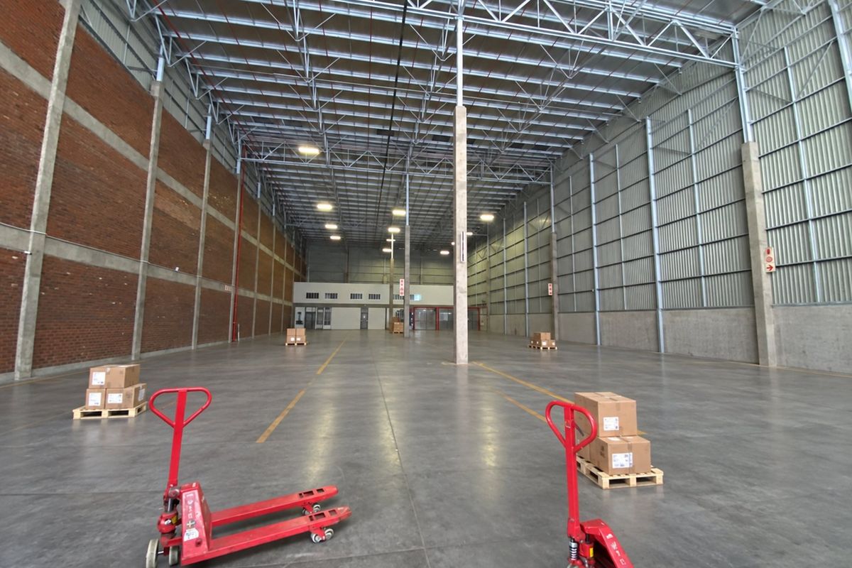 Spacious industrial warehouse unit featuring high ceilings with exposed steel trusses, concrete flooring, and a combination of brick and corrugated metal wall finishes.
