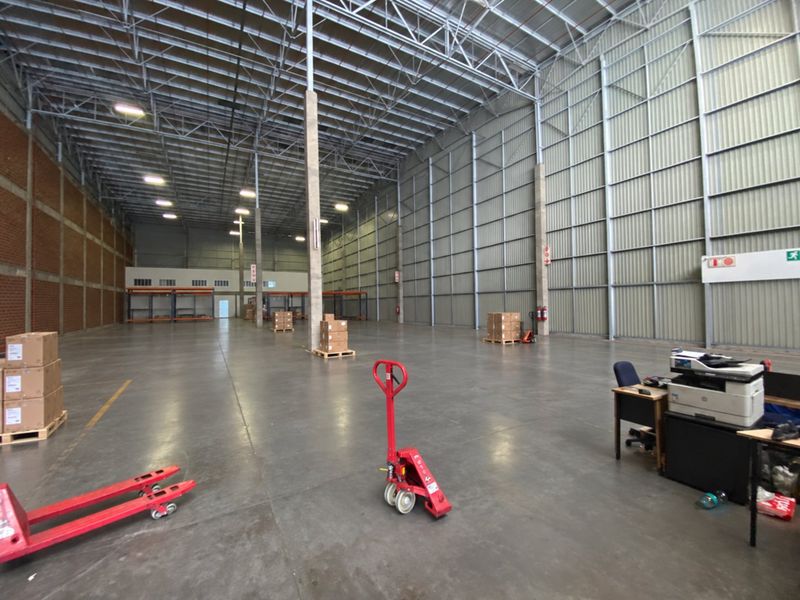 Spacious industrial warehouse featuring high ceilings with exposed steel trusses, polished concrete flooring, and metal wall cladding, suitable for storage or logistics operations.